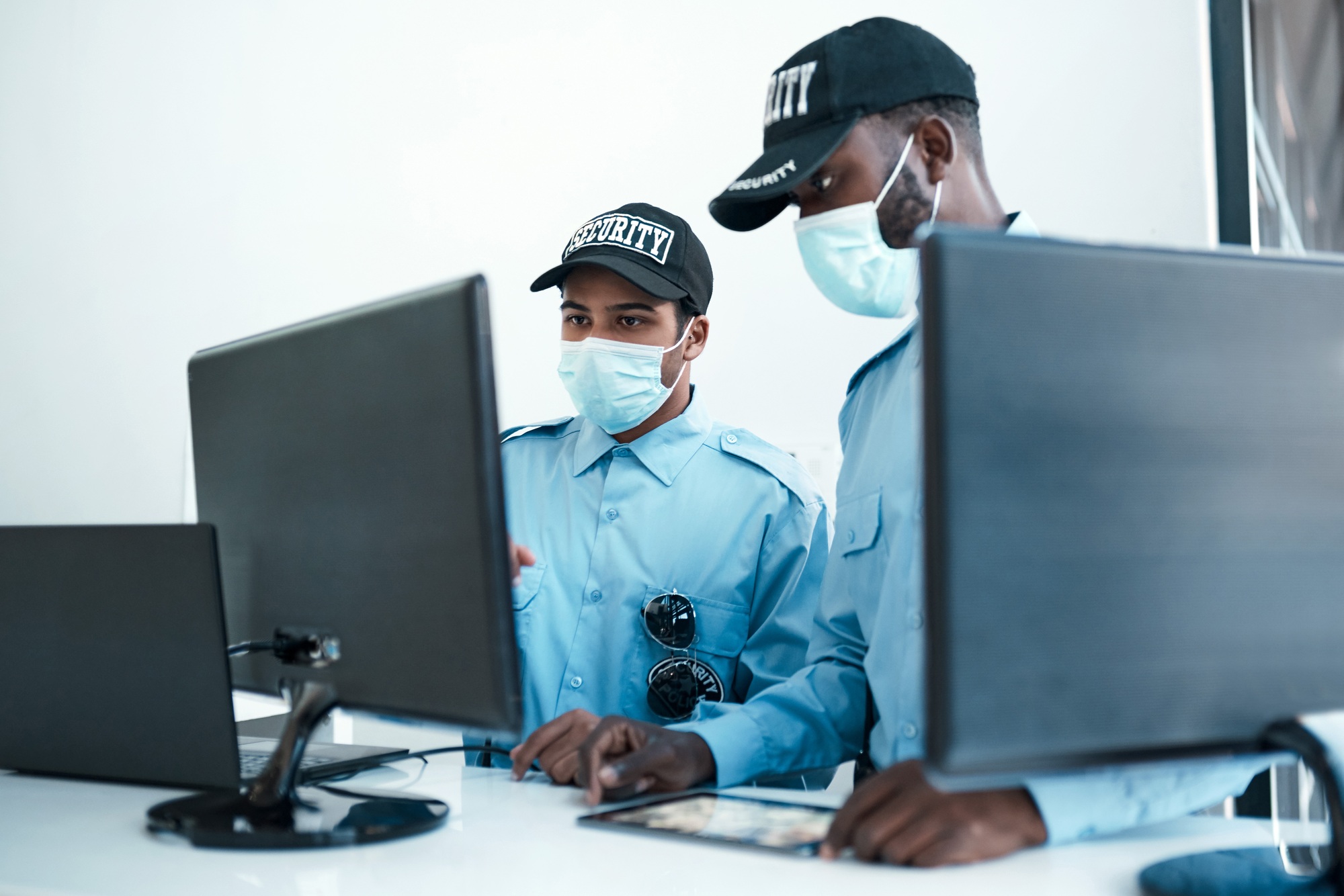 Shot of two masked young security guards on duty at the front desk of an office